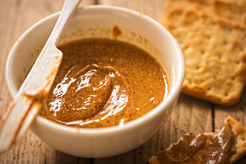 Almond butter in bowl with crackers on wooden table 