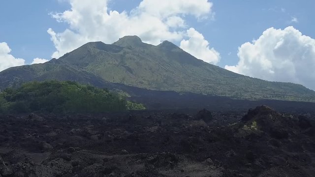 AERIAL ZOOM-IN EFFECT Rough stony black lava terrain and grey ashy volcanic soil at the toot of Mount Batur towards the peak of the mountain range. Dramatic landscape at Kintamani volcano crater, Bali