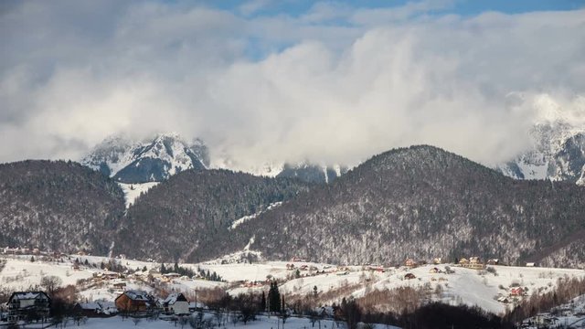 Winter view of Piatra Craiului Mountains from Pestera village in the morning. White dynamic clouds over Patra Craiului in background and winter countryscape of Pestera village in foreground. 4k timela