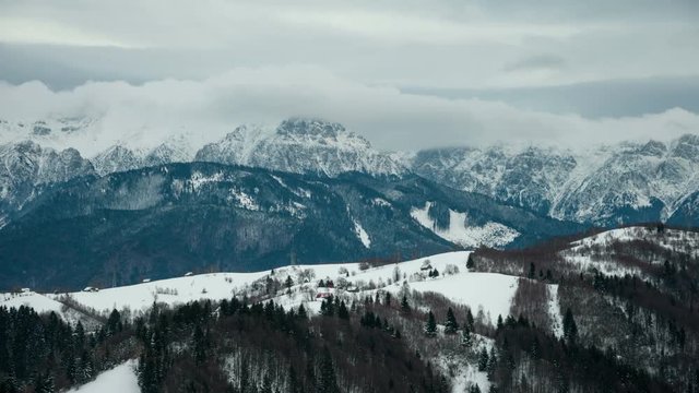 Winter view of Bucegi Mountains. Dynamic clouds revealing white mountains in background and isolated houses in foreground. 4k timelapse. 