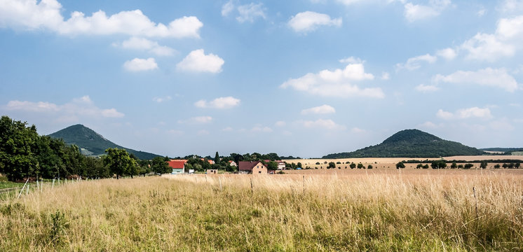 countryside with meadow, field, village, trees, isolated hills and blue sky with clouds