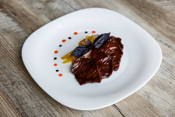 A white plate with slices of beef, stewed yellow pepper and onion. Purple basil on top. Drops of sauce.