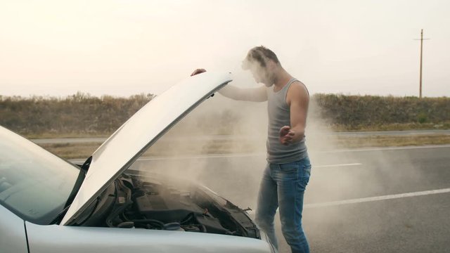 A man looks at a smoking engine of a broken car
