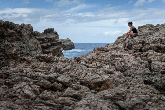 Mujer sentada en la montaña rocosa junto al mar reflexionando