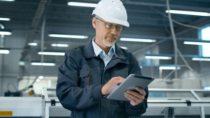 Senior engineer in hardhat is using a tablet computer in a factory.