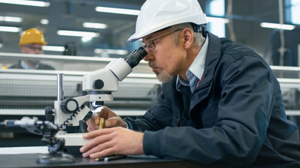 Naklejka na ściany i meble Senior engineer is inspecting a detail under microscope in a factory.