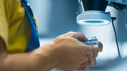 Engineer in a factory is inspecting a metal detail under a microscope with flashlight.