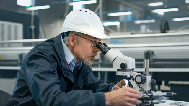Senior engineer is inspecting a detail under microscope in a factory.