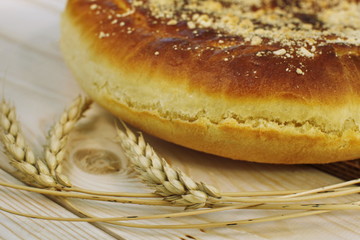 Ruddy baked onion and eggs pie with ripe wheat ears on wooden table close up