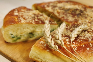 Ruddy baked onion and eggs pie with ripe wheat ears on wooden table close up