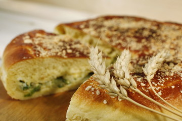 Ruddy baked onion and eggs pie with ripe wheat ears on wooden table close up