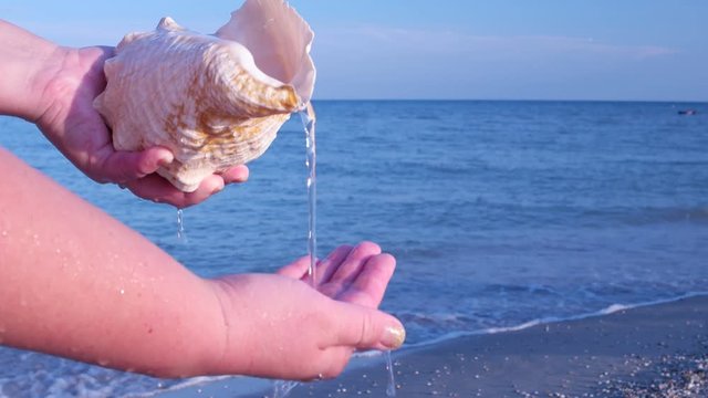The water flowing from the sea shell to the hand against the sea