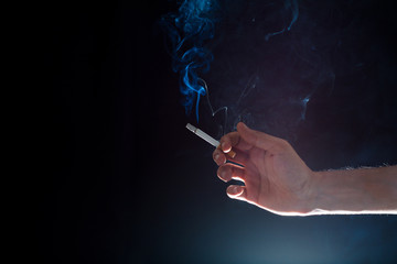 hand holding a smoky cigarette in a dark atmosphere