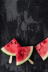 Fototapeta na wymiar watermelon slices on wooden sticks on a black background, top view, copy space