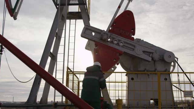 Camera Shows Worker Turning Level on Derrick at Back Light
