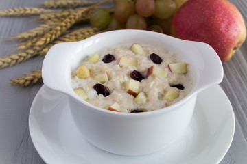 Healthy breakfast: oatmeal with milk, apple and raisins on the grey wooden background 