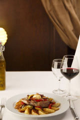 Pork and grilled vegetables arranged on a plate, Wineglass in the background, Traditional dish in elegant setting, Selective focus with soft light