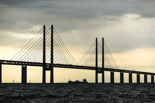 The Bridge Connecting Copenhagen And Malmo At Sunset With The Ship Underneath It.