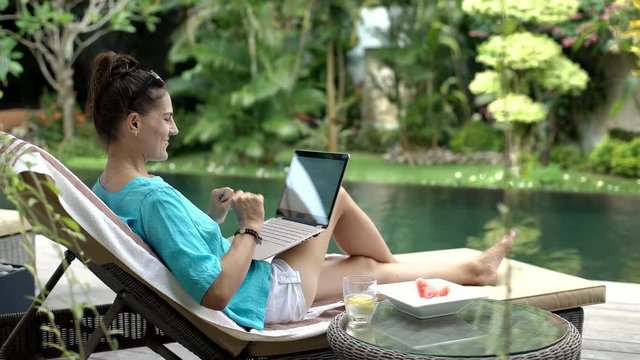 Attractive woman feels happy while finish using modern notebook next to the pool, steadycam shot
