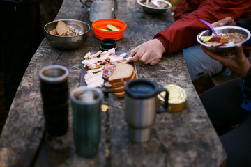 Photo of hiker's breakfast wooden table with bread, bacon , cans, other meals and hot mugs at the...
