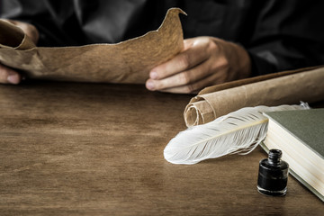 Man reading an old letter. Old quill pen, book and papyrus scroll on the wooden table. Historical atmosphere.