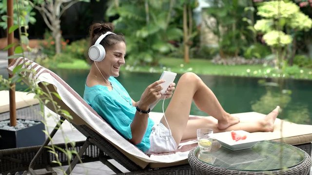 Woman wins while playing a game on tablet and relaxing next to the pool, steadycam shot
