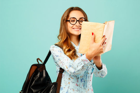 Pretty smiley girl wearing glasses pretty student holding books and wearing glasses over blue background