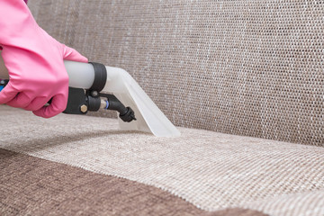 Sofa chemical cleaning with professionally extraction method. Hand in rubber protective glove holding nozzle of extractor. Upholstered furniture. Early spring or regular clean up.