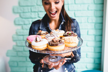 Beautiful young woman enjoying in delicious glazed and decorated donuts