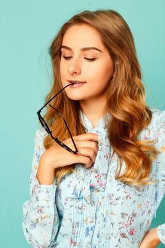 Pretty thoughtful girl with glasses in her mouth over blue background
