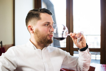 Fototapeta na wymiar Young attractive man sitting at the table and drinking wine from a glass in restaurant
