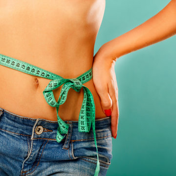 Woman measuring her waist over blue background. Wellness concept.