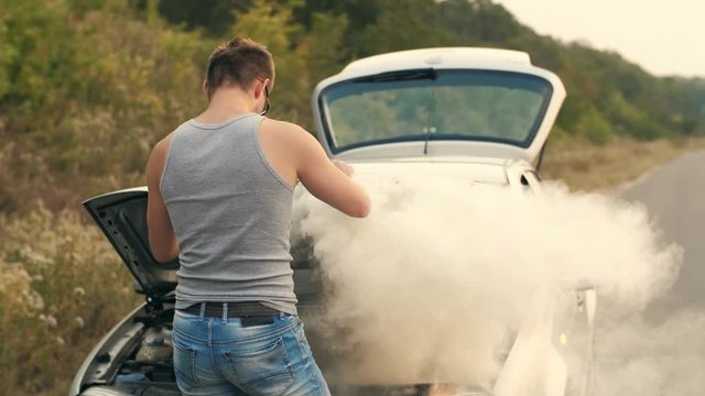 A man looks at a smoking engine of a broken car