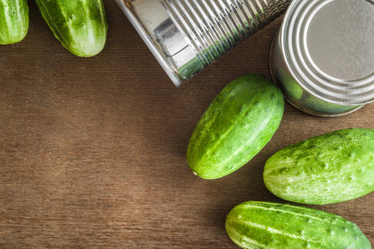 Green cucumbers with metallic cans on the table. Preserved vegetables. Healthy eating and lifestyle. Rustic atmosphere. Top view.