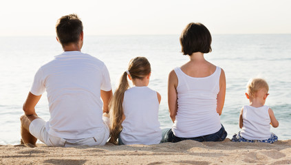 Man and woman with kids sitting with back to camera on  beach