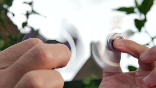 Hand holding popular fidget spinner toys on sky background 