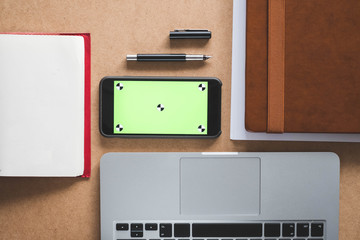 topdown shot of a table with a phone with green screen and a laptop computer