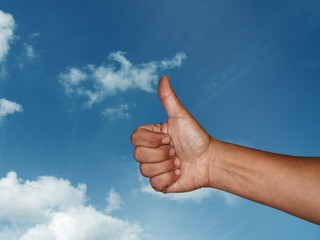 Hand mit Daumen hoch vor blauem Himmel mit wei&szlig;en Wolken