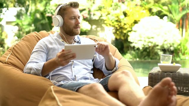 Man listening music and eating fruits while relaxing next to the pool
