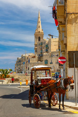 Horse carriage on the street of old town and St. Paul's Anglican Pro-Cathedral in Valletta, Malta