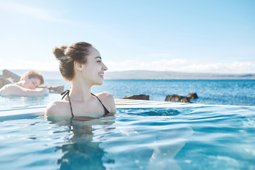 Fototapeta na wymiar Young cheerful girl swimming in water of pool looking away on background of sea, Iceland, West Fjords. back view