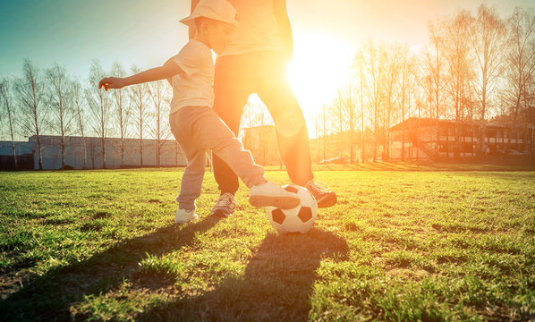 Father and son playing together with ball in football under sun