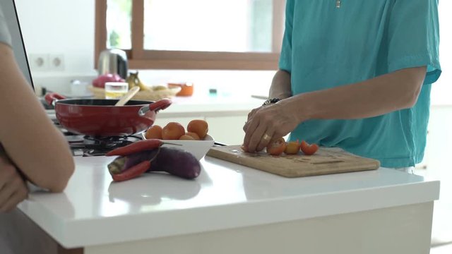 Woman standing with someone in the kitche and cutting tomatoes, steadycam shot
