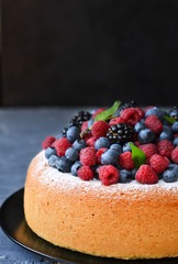 Vanilla cake with creamy cream and berries: blueberries, raspberries and blackberries on a concrete background.