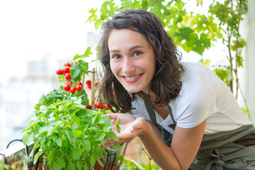 Young woman taking care of her plants and vegetables on her city balcony garden - Environment and...
