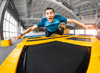 Fototapeta na wymiar A young fit happy man jumping and flying on trampoline in fitness gym