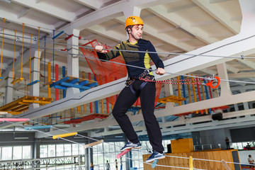 Young man climb with rope belay and helmet at indoors amusement rope park