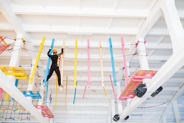 Young man climb with rope belay and helmet at indoors amusement rope park