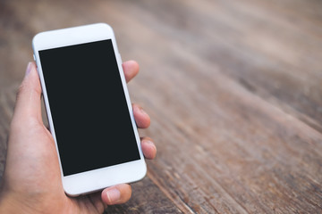 Mockup image of a man's hand holding white mobile phone with blank black screen on vintage wood table in cafe
