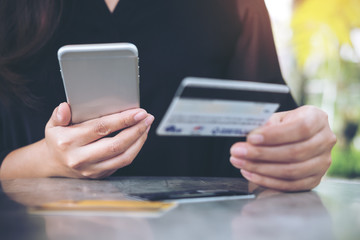 Closeup image of a woman's hand holding credit card and using mobile phone on the table in office